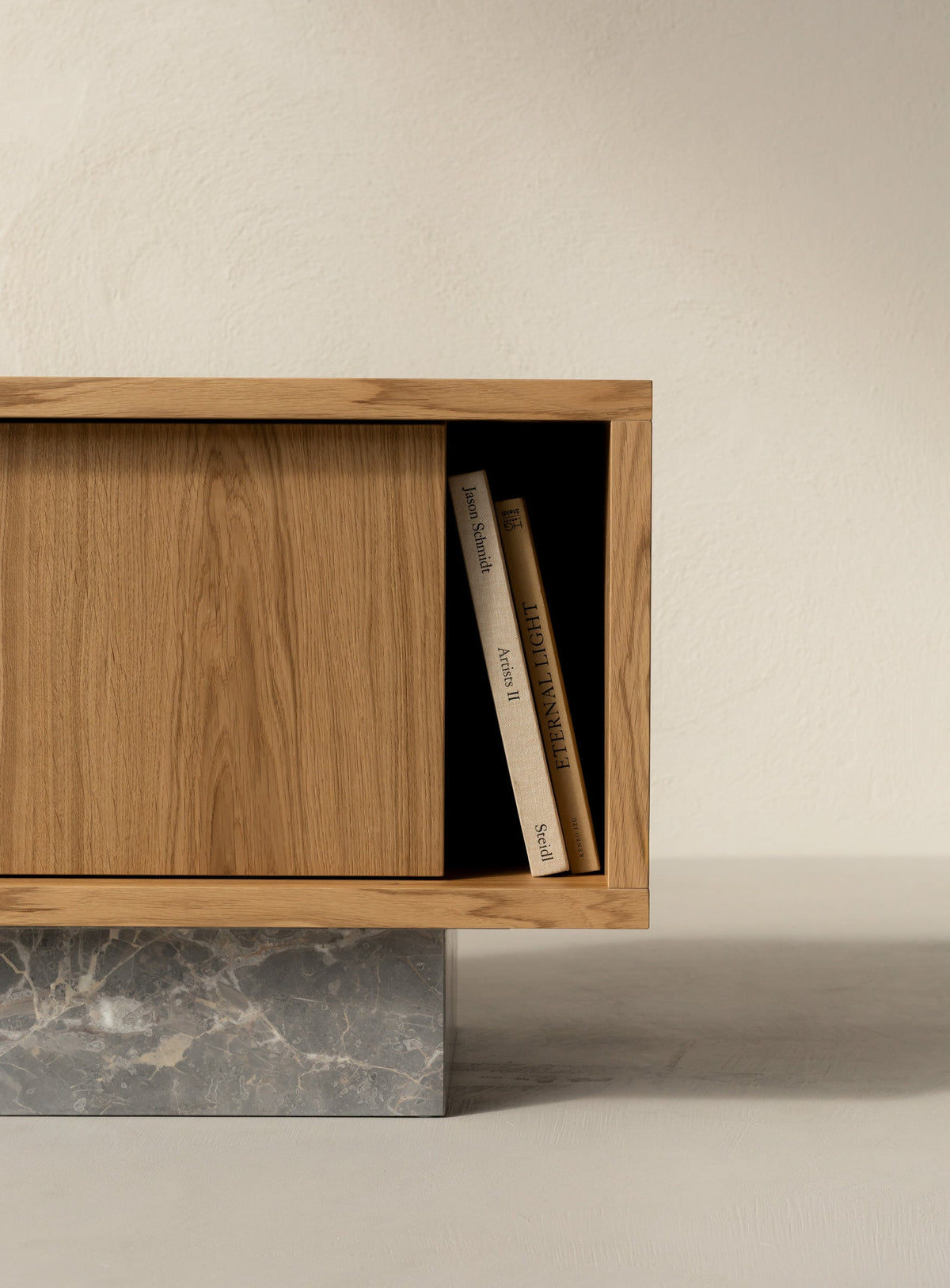 Detail of the BLOCK Side Table's open niche holding art books, natural oak body on a brushed Fior di Bosco marble base.