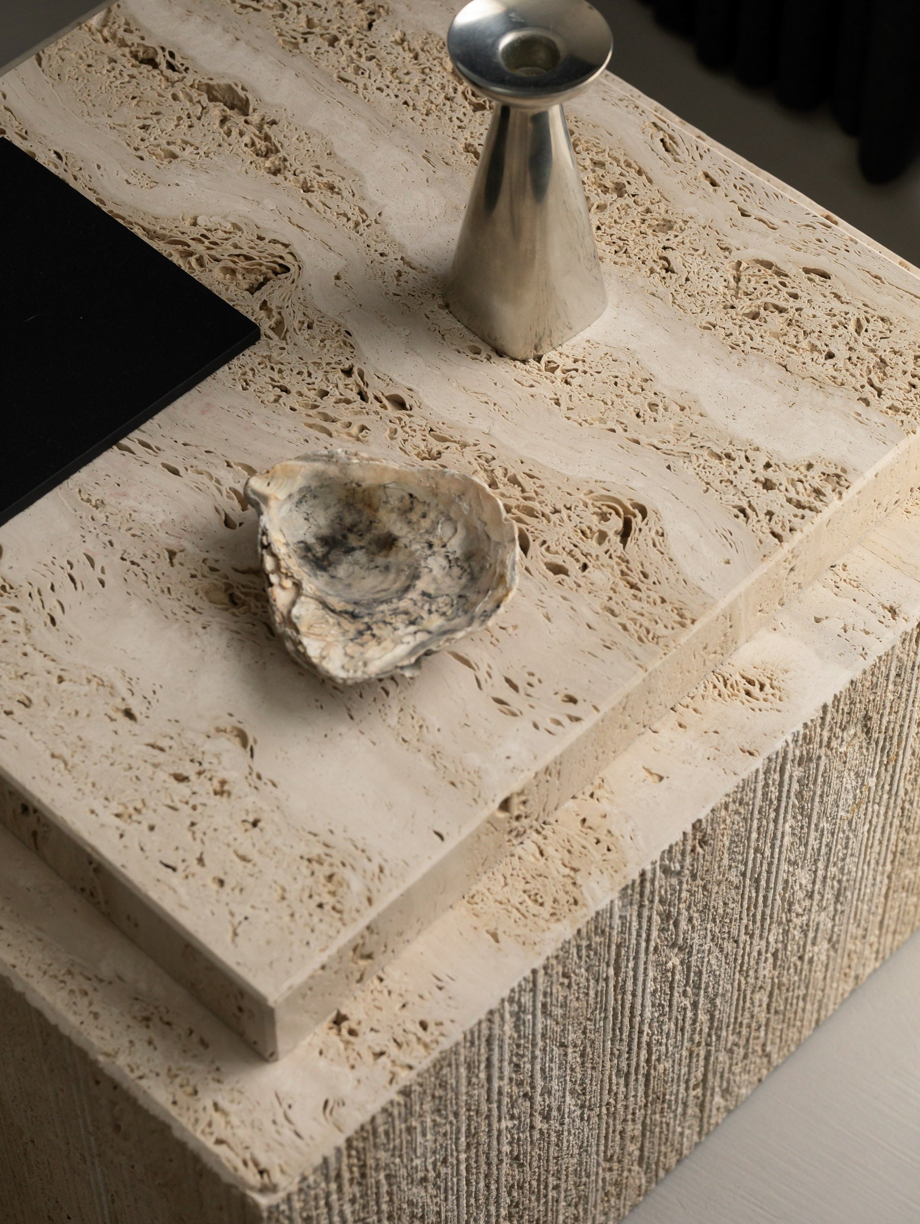 Detail of the Un'common BARI travertine coffee table's surface, styled with a shell and a brushed metal cone vase, showing the natural stone veining.