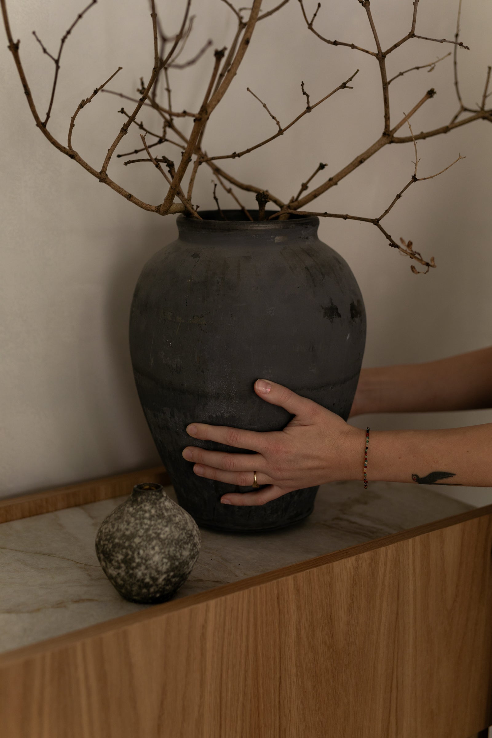Hands arranging a large ceramic vase on a natural marble console table with an oak base in a minimalist interior.