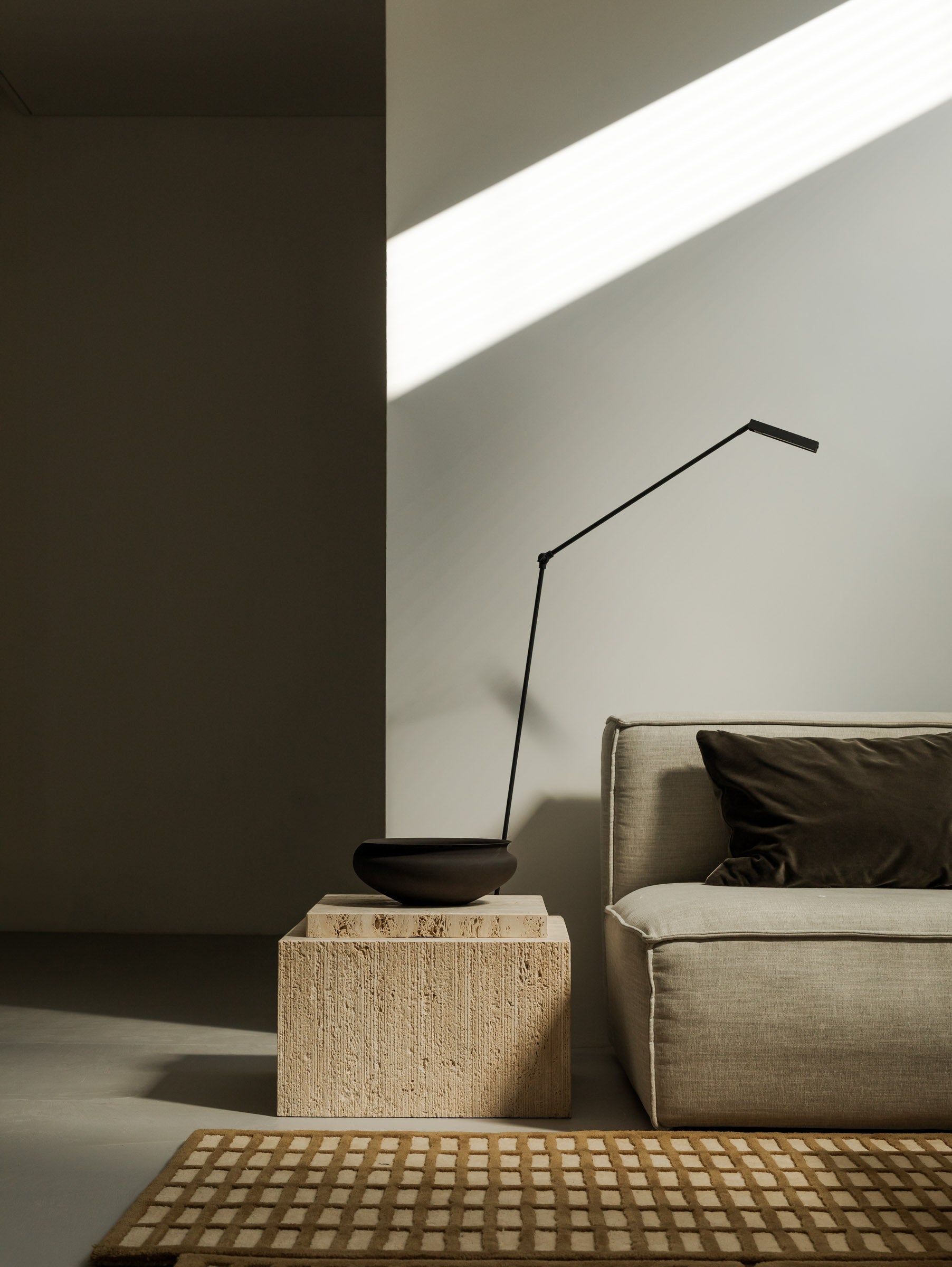 Un'common BARI travertine coffee table in a dark, moody corner setting with a floor lamp.